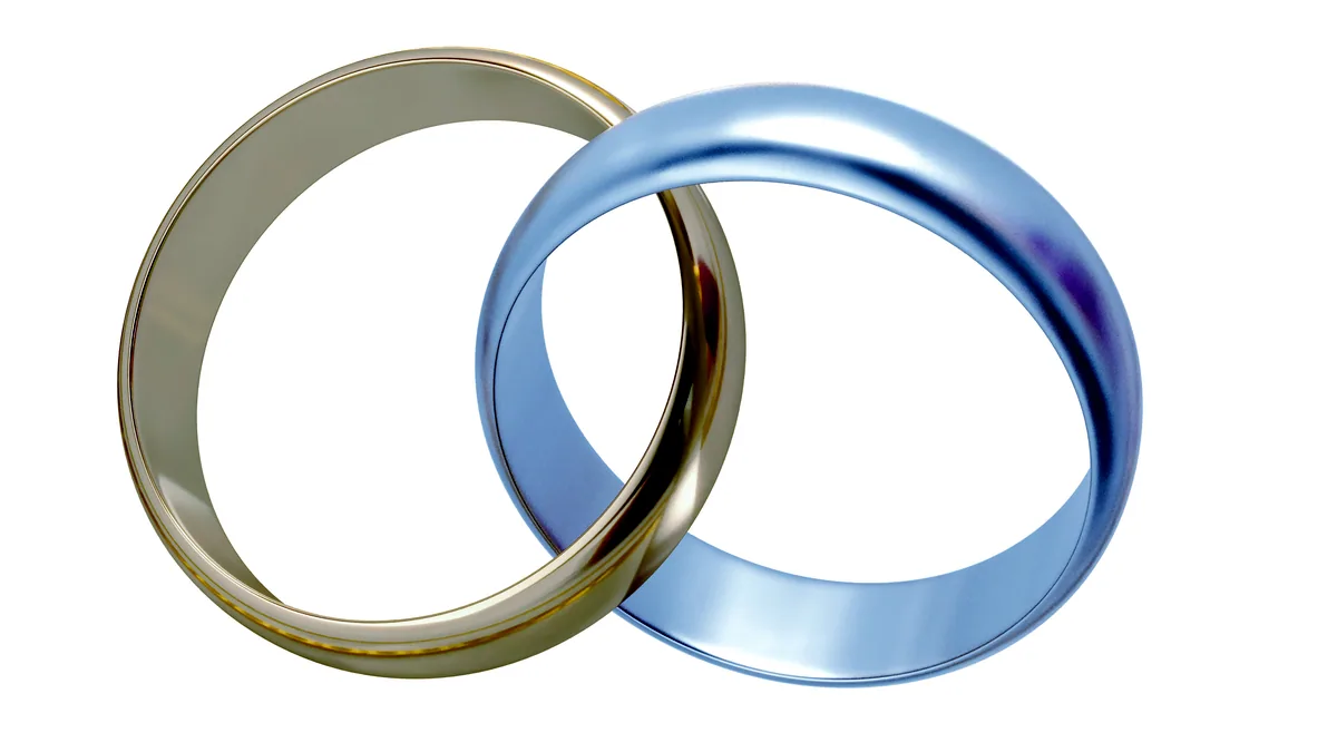 A gold ring and a silver ring placed side by side on a charcoal tile, warm and cool tones contrasting.