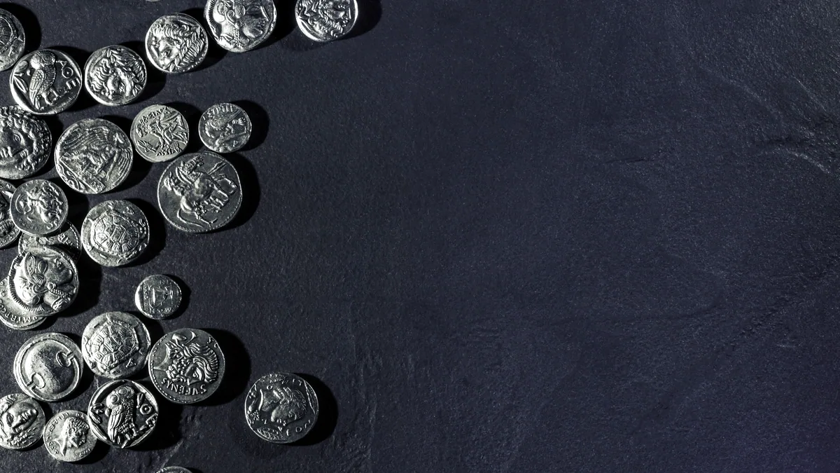 A small pile of silver coins scattered on dark slate, their edges glinting under cool studio light.