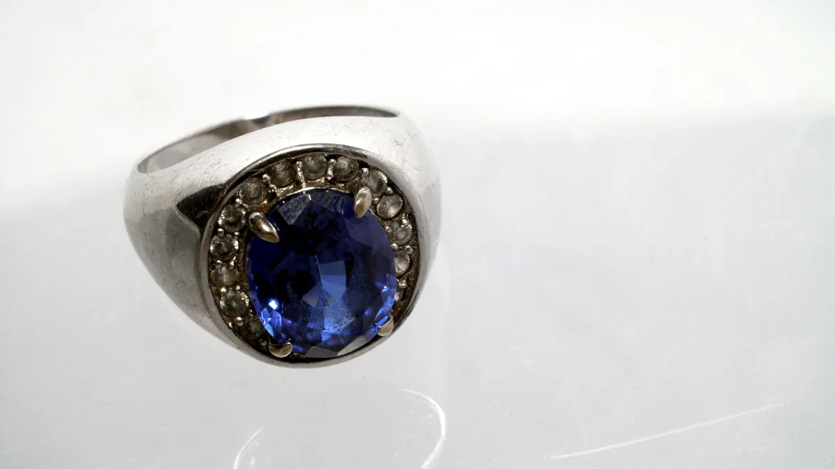 A silver ring set with a deep blue gemstone, the stone glowing softly against the dark charcoal ground.