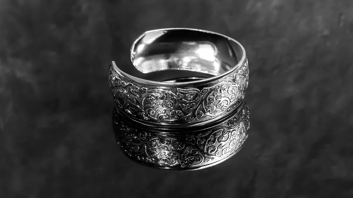 A heavily carved gothic silver ring with pointed arch detailing, its relief shadows deep on a dark tile.