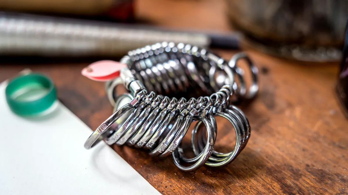A hand-finished silver ring beside a pair of fine pliers on a dark workbench, both under one lamp.