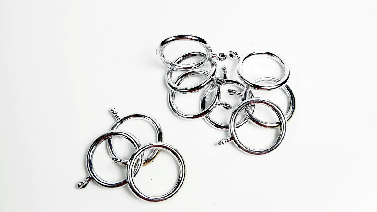 A cluster of small open silver jump rings scattered on a dark surface, each catching a sliver of light.