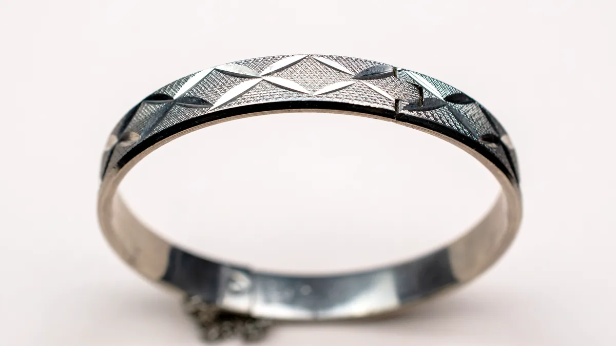A wide brushed silver band ring standing upright on a dark surface, catching a single cool light.