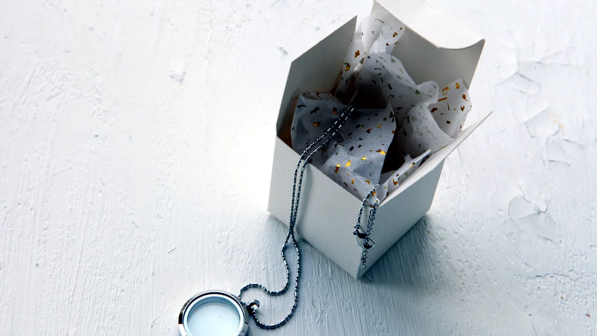 A silver necklace resting inside an open dark gift box, the chain arranged in a neat loop on velvet.