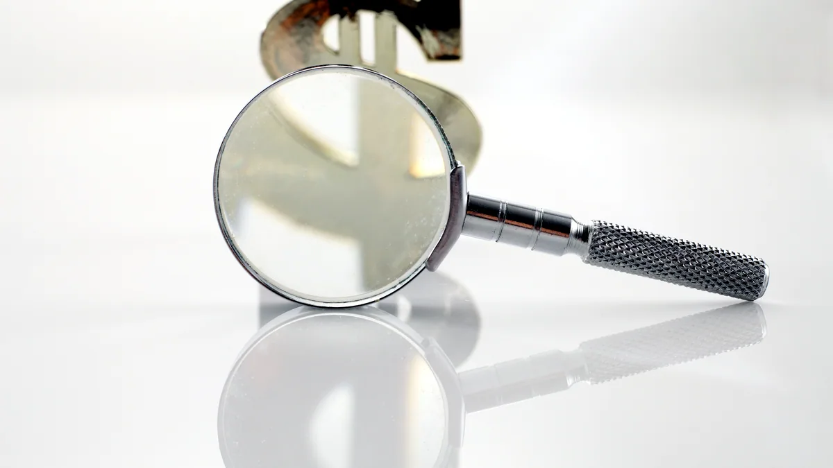 A magnifying glass held over a small silver hallmark, the stamped mark sharp beneath the lens.