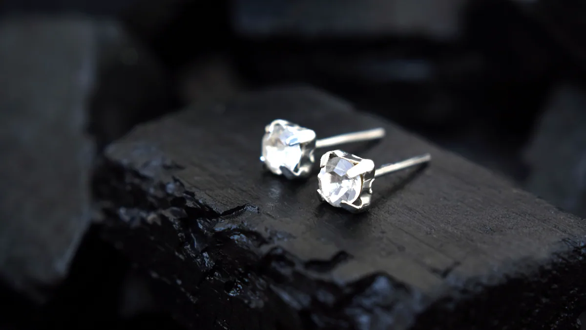 A pair of small silver stud earrings hanging from a dark display card, their backs glinting under cool light.