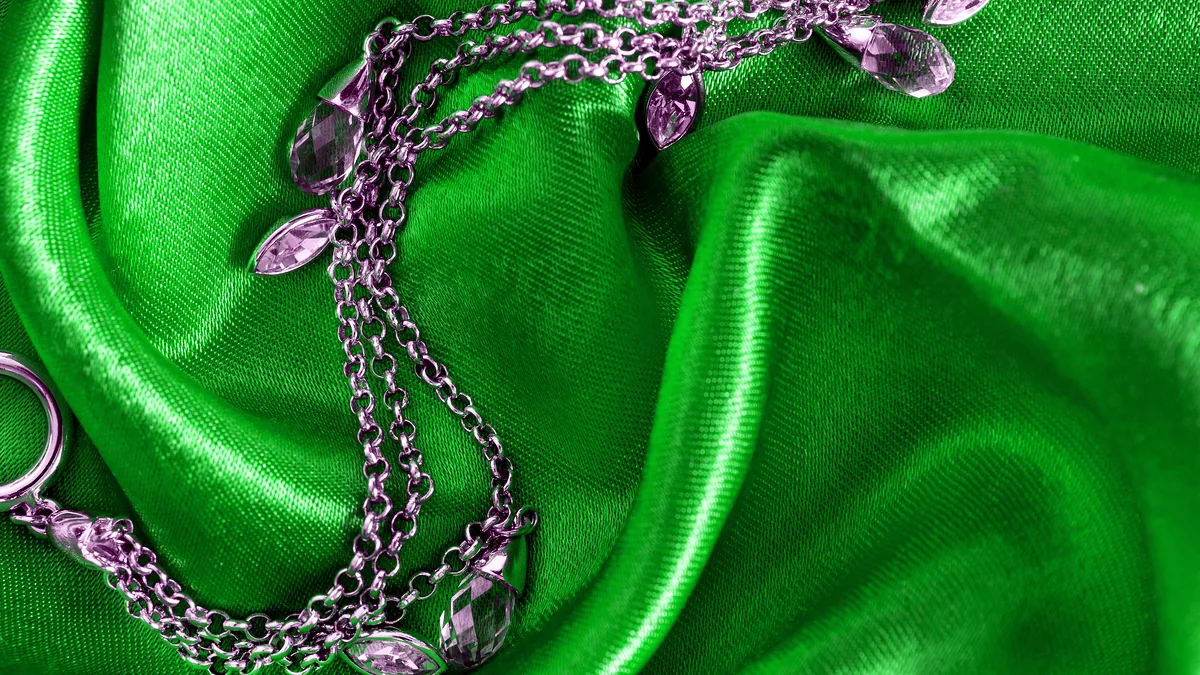 A fine silver chain necklace draped in a gentle curve over a dark display stand, links catching individual highlights.