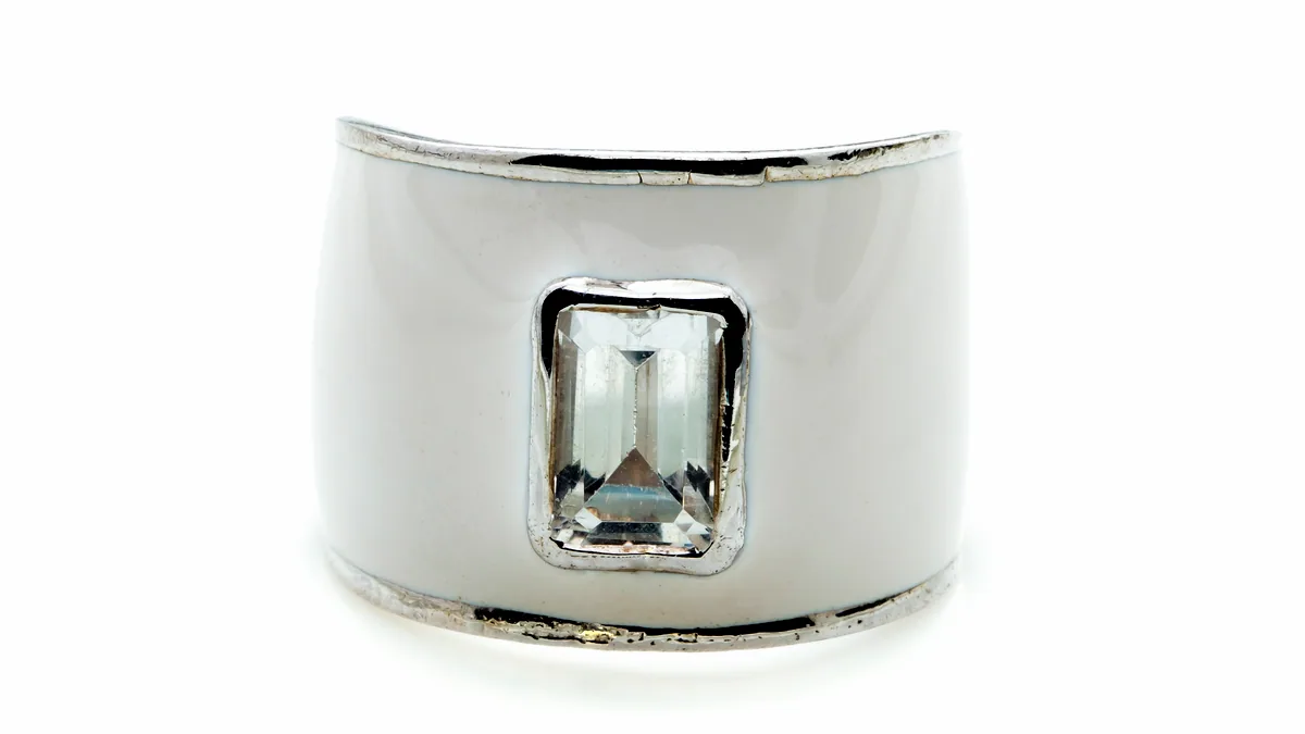 A tiny silver toe ring with a small clear stone, photographed at a low angle on dark charcoal.
